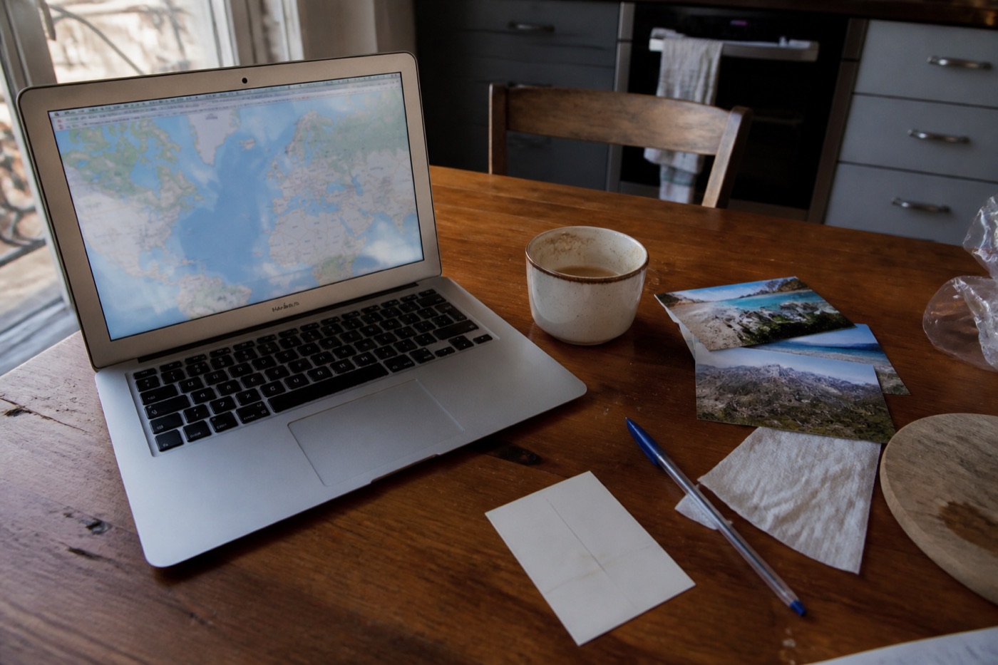 Notebook s cestovní trasou na mapě, fotografiemi a pohlednicí na kuchyňském stole