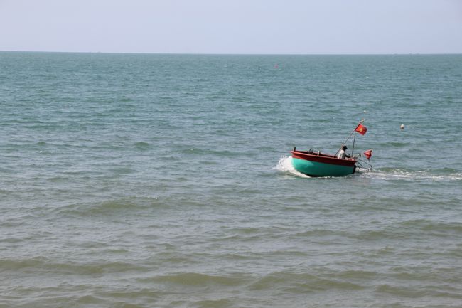 A basket boat with the Vietnamese flag passes by on the beach in Mui Ne