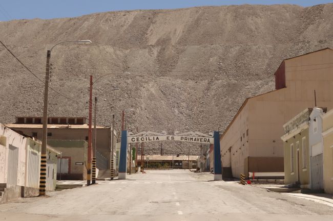 Das eigentliche Dorf Chuquicamata ist laengst verlassen. Ein grosser Teil der Stadt wurde auch schon mit dem Abraum aus dem Bergbau zugeschuettet. Das ist der riesiege Berg im Hintergrund. Die Haeser wurden einfach zugeschuettet. Die aelteren Berge schimmern noch etwas gruenlich, da vor ein paar Jahrzehnten noch nicht alles Kupfer gewonnen werden konnte. Dieses Erdreich wird heute nochmals gereinigt um auch das Restkupfer noch zu gewinnen.