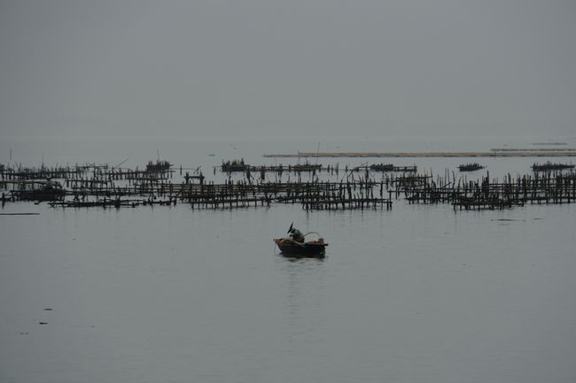 Fischerboot auf dem Wasser mit Muschelzucht im Hintergrund