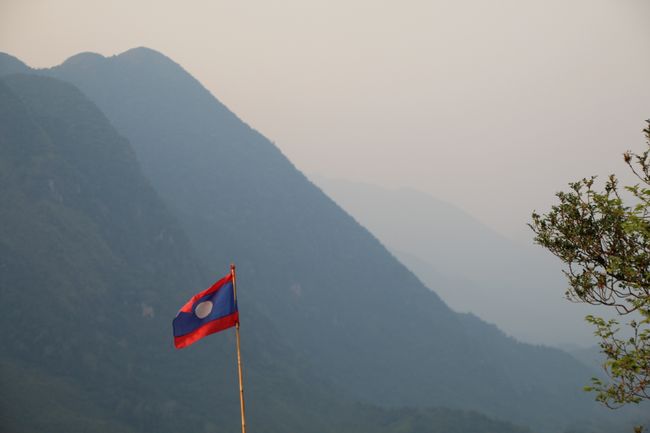 Berglandschaft in leichtem Nebel, im Vordergrund die laotischer Flagge an Bambus befestigt
