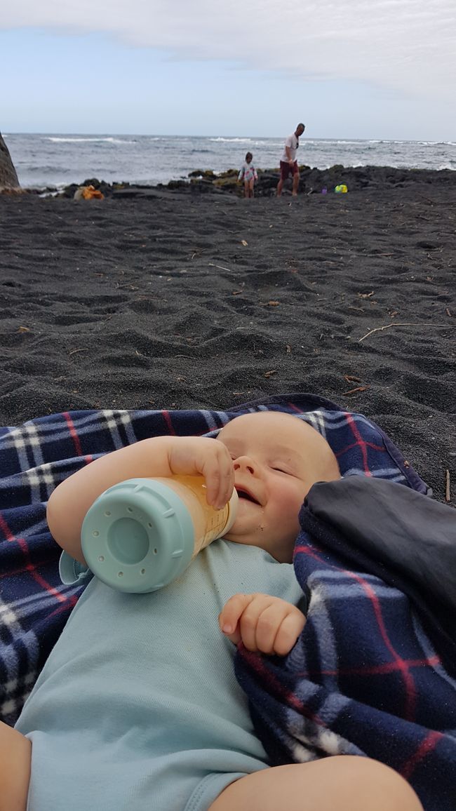 Glückliches Baby am schwarzen Strand
