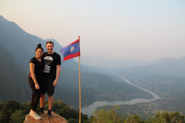 Jonas sitting next to the Laotian flag in front of giant mountains
