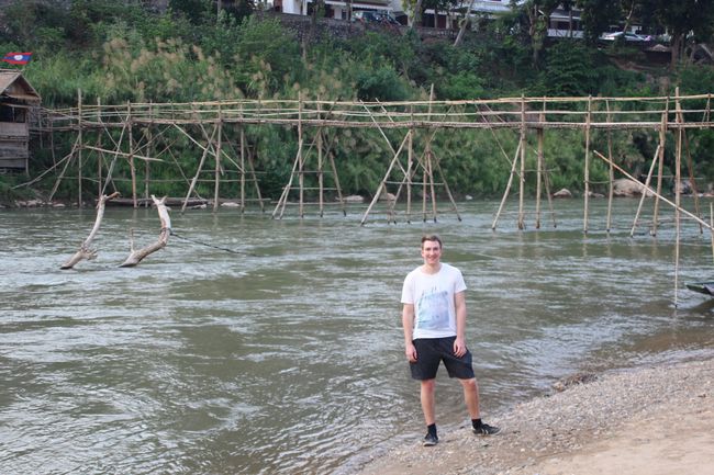 Jonas standing on the banks of the Nam Khan River in front of the bamboo bridge