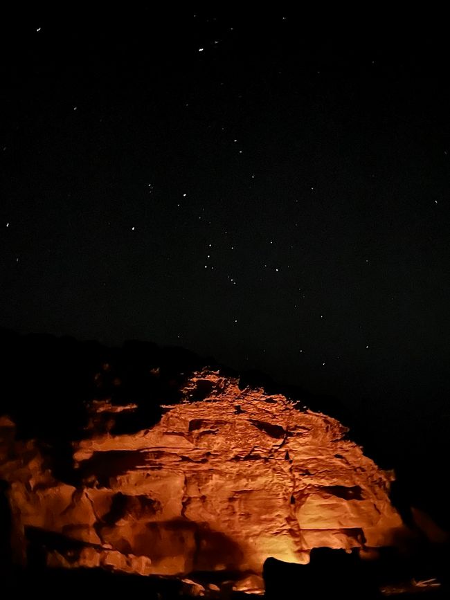 Orion above the cliffs illuminated by the campfire
