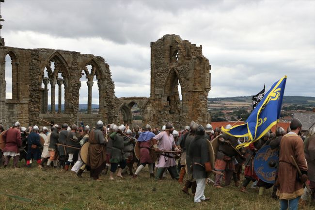 Men dressed in medieval costumes reenact a battle in front of the ruins
