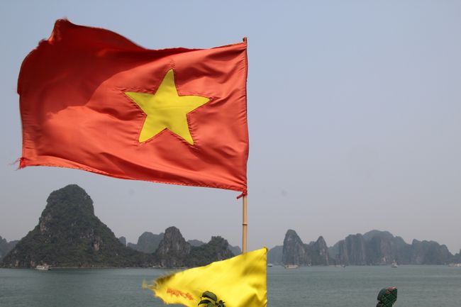 Vietnamesische Flagge vom Schiff weht im Wind mit Bai tu Long Bay im Hintergrund
