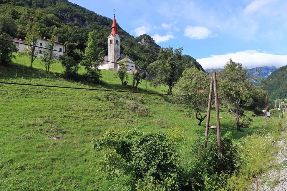 Die Ortschaft Grahovo ob Bači. Im Hintergrund sind wolkenverhangen die Julischen Alpen zu sehen.