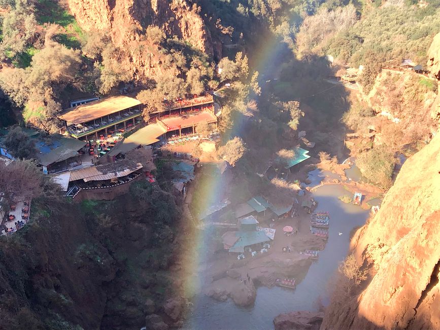 A rainbow spans the valley at the foot of the waterfall.