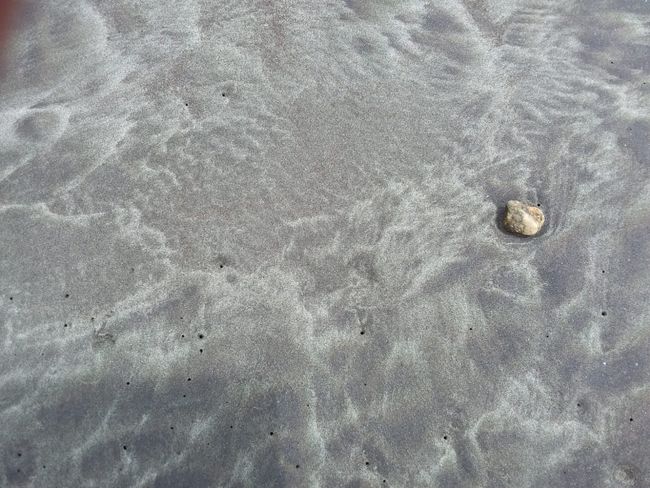 Der Sand am Strand ist grau, schwarz und lila. Die Wellen geben ihm eine sehr eigene Struktur. Das Meer malt....