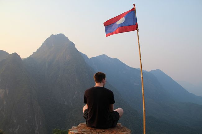 Franzi sitting next to the Laotian flag in front of giant mountains