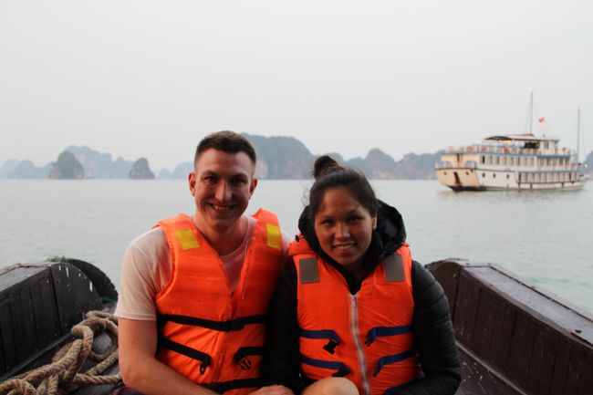 Wir beide auf dem kleinen Boot, haben Schwimmwesten an und im Hintergrund ist die Bai tu Long Bay